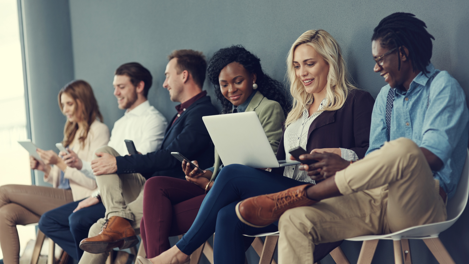 group of young adult sitting in a row looking at their phones and laptops